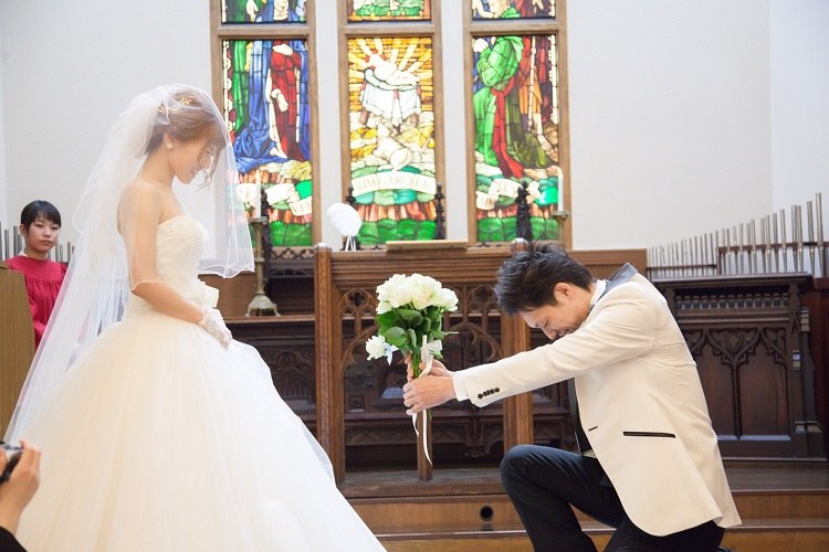 結婚式の人前式でゲストから集めた12本の白いバラの花束を差し出して跪いてプロポーズする新郎